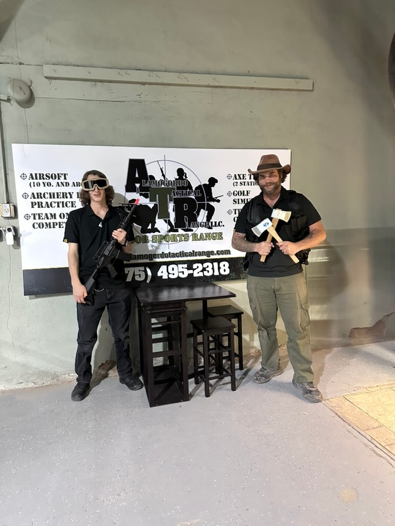 Two ATR staff members posing in front of the ATR banner with airsoft rifle and axe