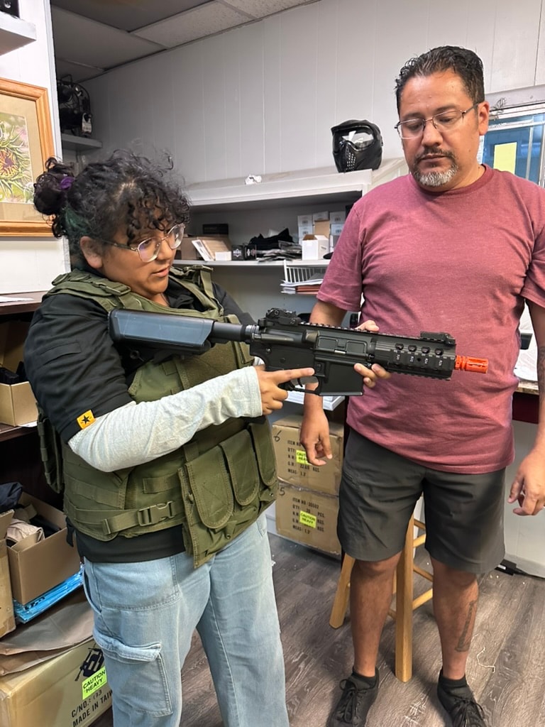 Player in tactical vest holding an airsoft rifle with an ATR staff member at the range