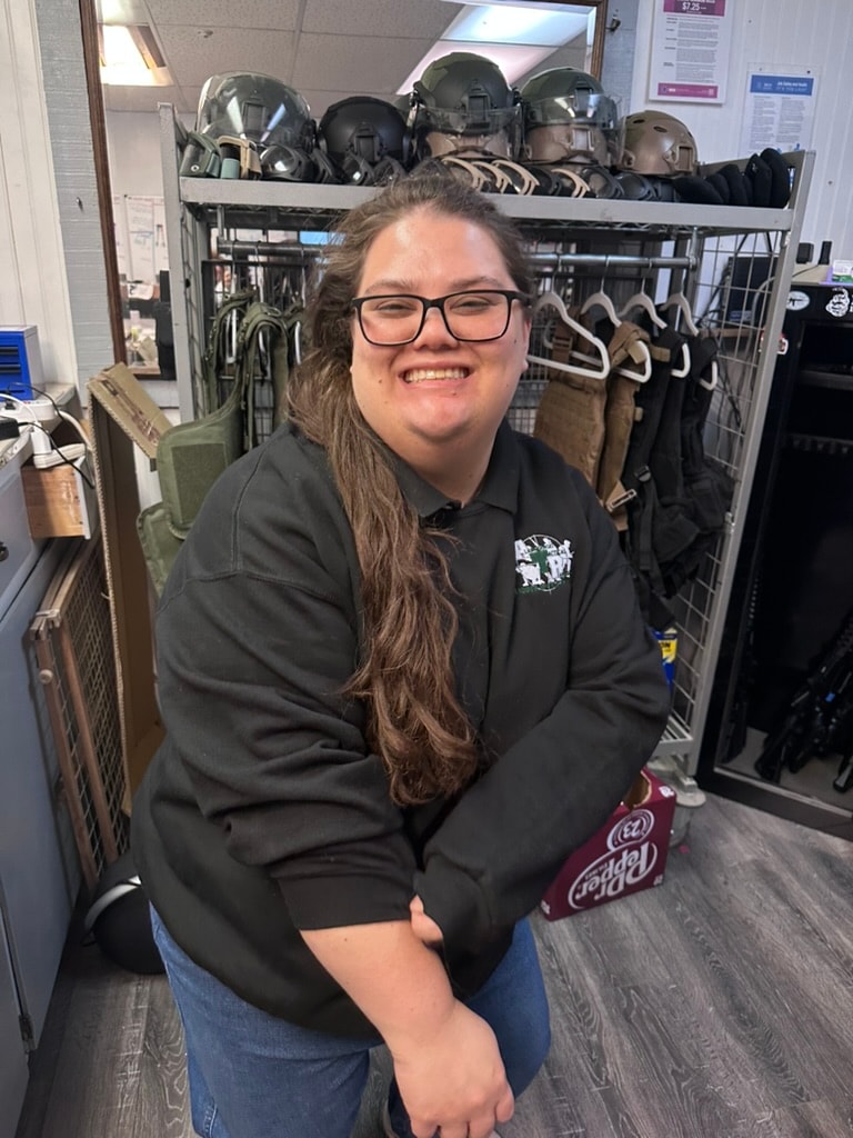ATR staff member smiling in the gear room in front of helmets and tactical vests